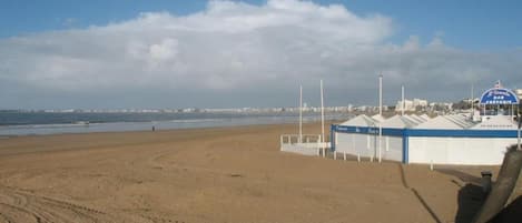 A beach with a row of beach huts and a clear sky.