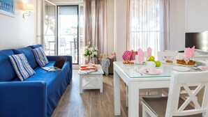 Una sala moderna con un sofá azul, una mesa de comedor para dos personas y un ventanal con cortinas.