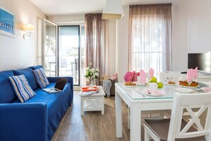 A modern living room with a blue sofa, a dining table set for two, and a large window with curtains. - Apartment in La Baule with Sea View (PORNICHET)