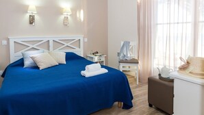 Habitación de hotel con cama, mesita de noche, una silla y una mesa con sombrero y tetera.