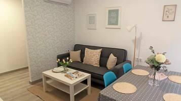 A living room with a sofa, a coffee table, a dining table with chairs, and a small vase with flowers.