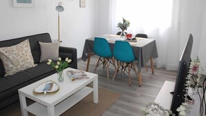 A living room with a sofa, a coffee table with magazines, a dining area with a table and chairs, and a TV on a stand. - Apartment amb Balcó (Consuegra)