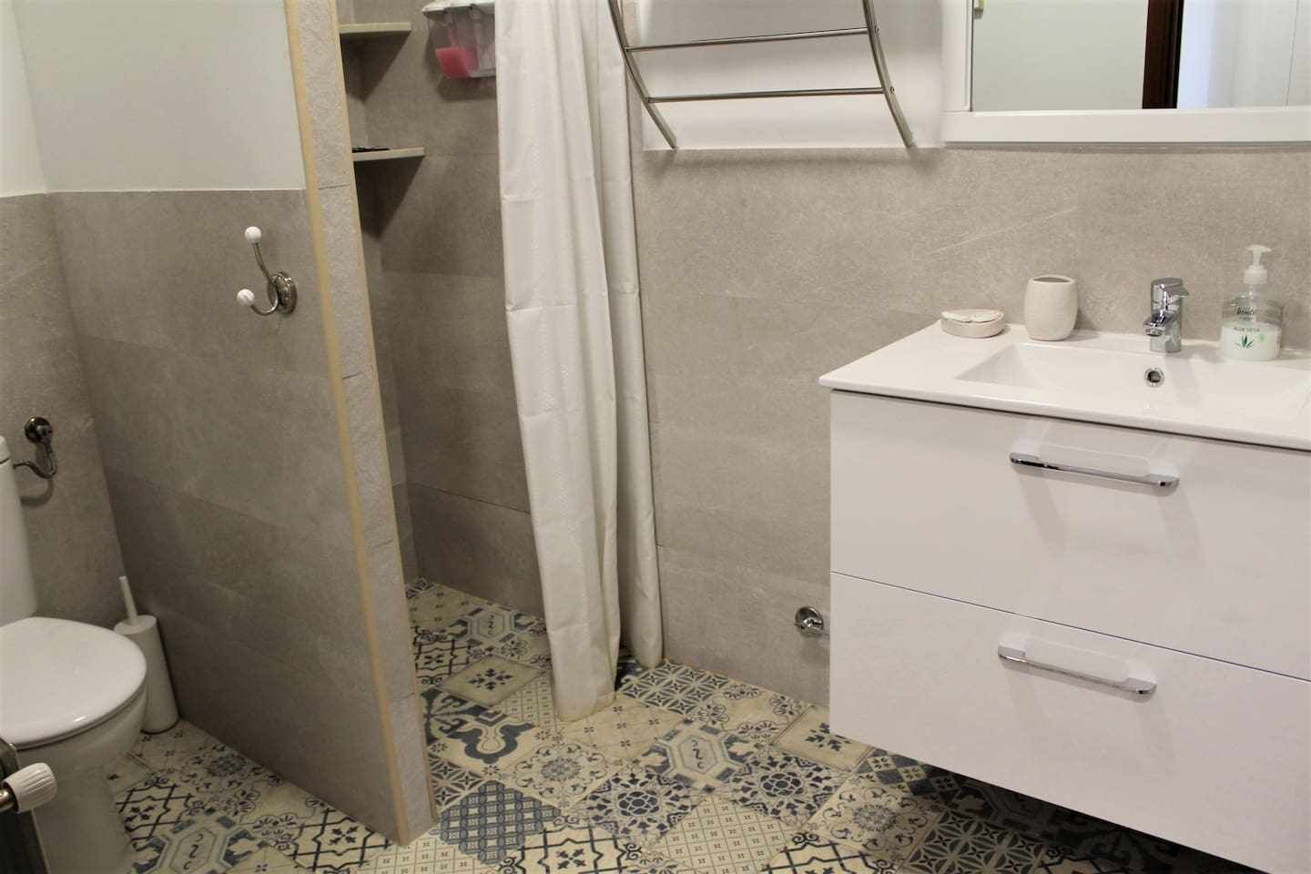 Un baño con inodoro, lavamanos con espejo y zona de ducha.