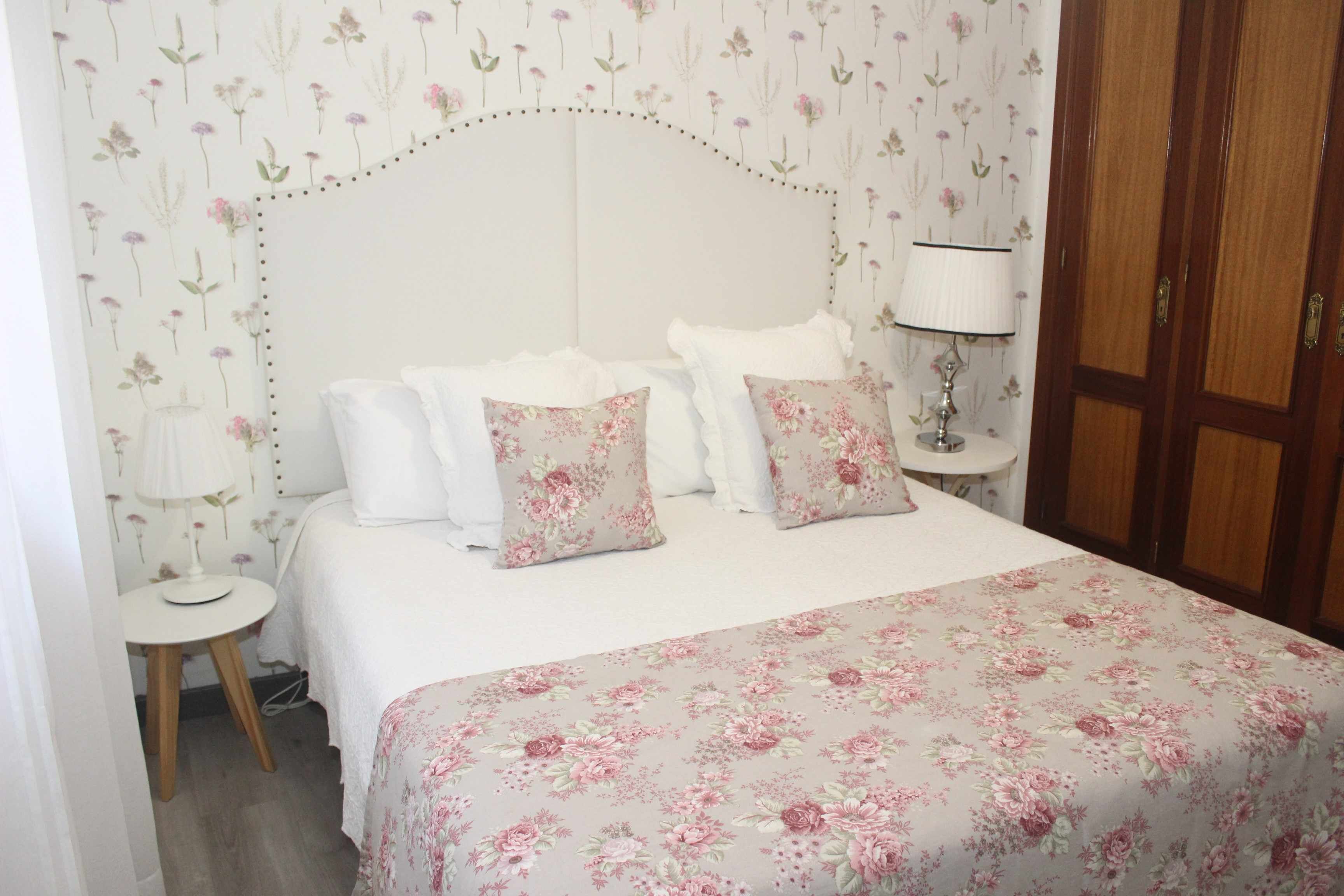 Een slaapkamer met een sprei met bloemenprint, een wit hoofdbord en een nachtkastje met een lamp.
