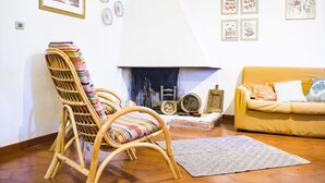 A living room with a fireplace, a wicker chair, a sofa, and wall art. - S'Omu e Mari by All4sardinia  (Cardedu)
