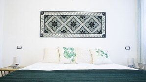 A neatly made bed with a green blanket, a decorative wall hanging, and two bedside lamps. - S'Omu e Mari by All4sardinia  (Cardedu)