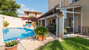 A residential property with a swimming pool, outdoor seating, and a covered patio area.