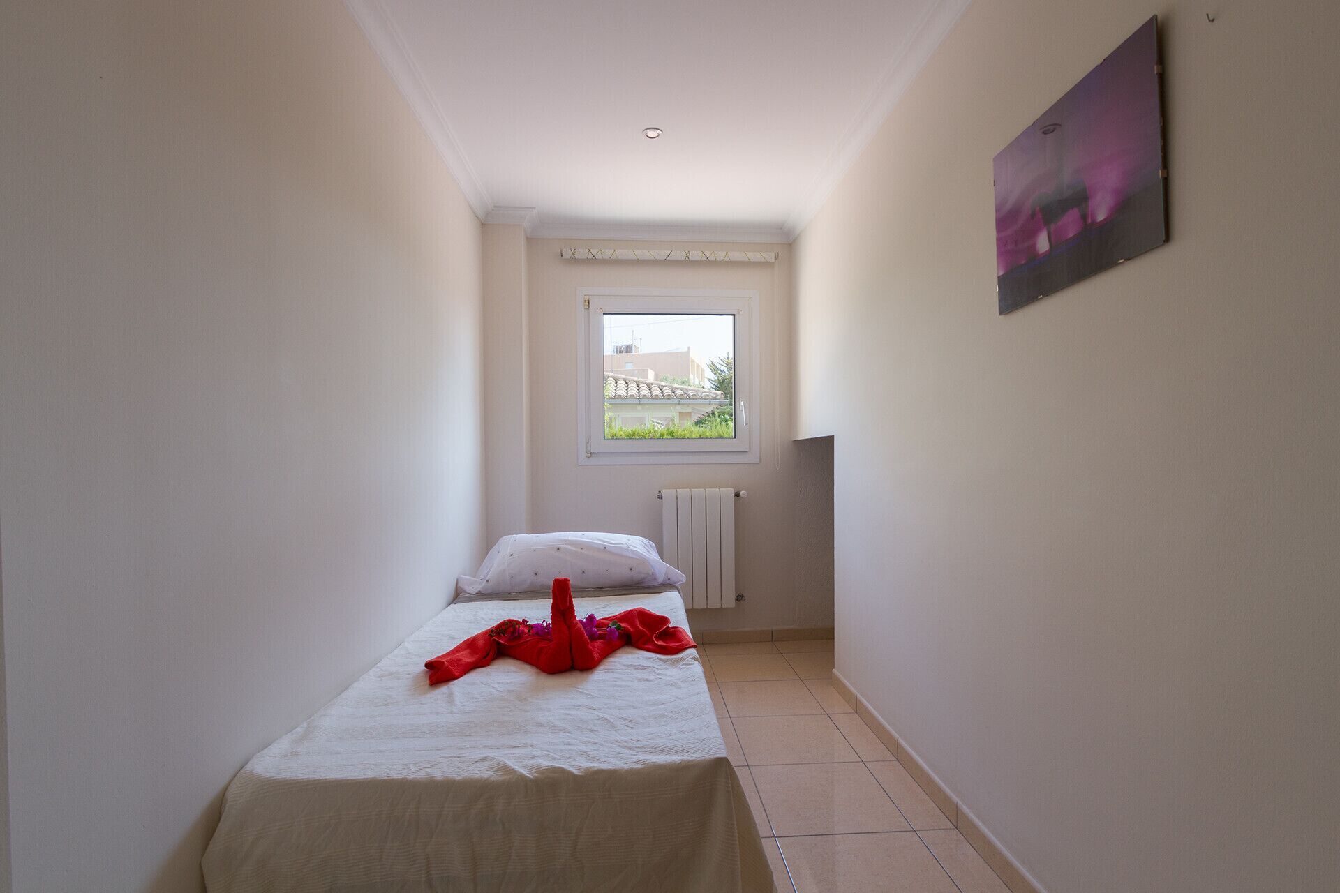 A narrow room with a bed, a radiator, and a window.