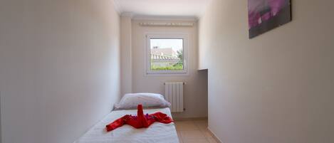 A narrow room with a bed, a radiator, and a window.