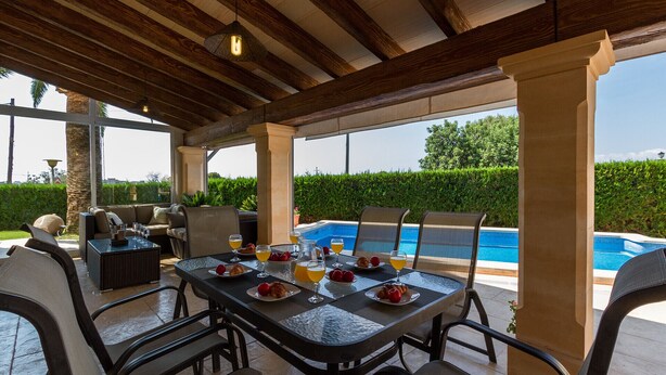 An outdoor dining area with a pool view, featuring a table set for breakfast with drinks and pastries.