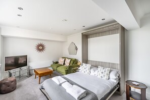 A modern hotel room with a bed, a green armchair, a small table, a TV, and a decorative wall piece. - Cocoa Suites 45 - York city centre studio (sleeps 2) (York)