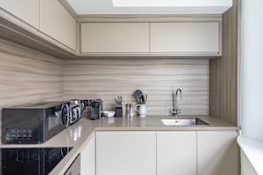 A compact kitchen with a microwave, toaster, and coffee maker on the counter, a sink, and cabinets with a light wood finish. - Cocoa Suites 45 - York city centre studio (sleeps 2) (York)