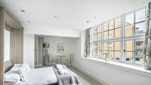 A modern hotel room with a bed, a small table, chairs, a window with a view of buildings, and a door leading to a balcony. - Cocoa Suites 45 - York city centre studio (sleeps 2) (York)