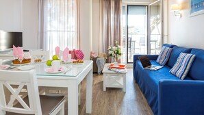 A modern living room with a blue sofa, a dining table set with plates and glasses, and a television on a white stand. - Sea Breeze Stay w/ Pool (PORNICHET)