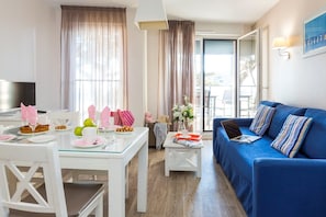 Ein modernes Wohnzimmer mit einem blauen Sofa, einem Esstisch gedeckt mit Tellern und Gläsern sowie einem Fernseher auf einem weißen Schrank.