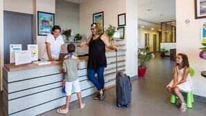 A reception area with a counter, a woman assisting a child, and another woman sitting on a stool. - Sea Breeze Stay w/ Pool (PORNICHET)
