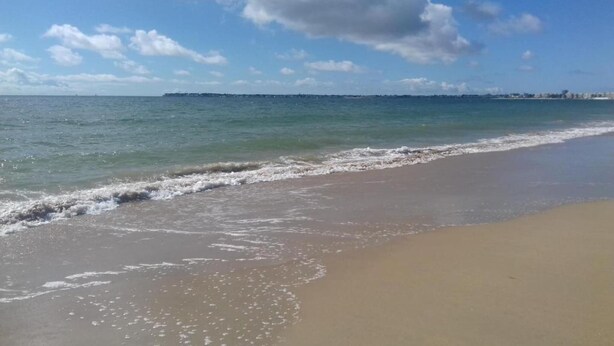 Uma praia com areal arenoso e ondas suaves.