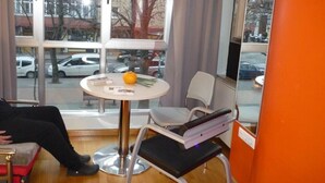Une pièce avec une grande fenêtre, une table ronde avec une chaise, et une personne assise sur un canapé.