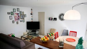 Ett vardagsrum med en soffa, ett soffbord med frukt, en tv och en matplats med stolar och ett bord.
