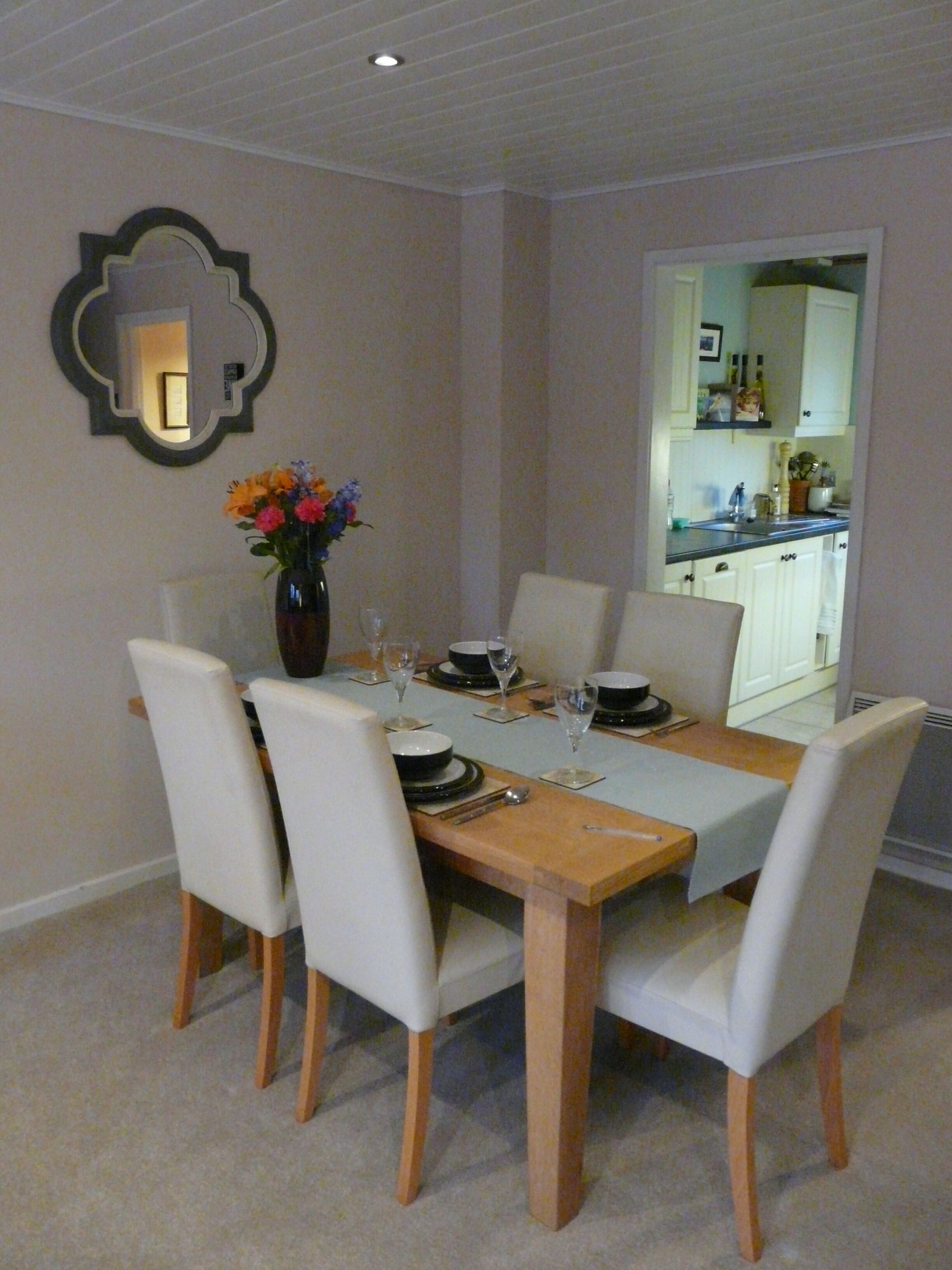 A dining area with a wooden table set for four, white chairs, and a vase with flowers.