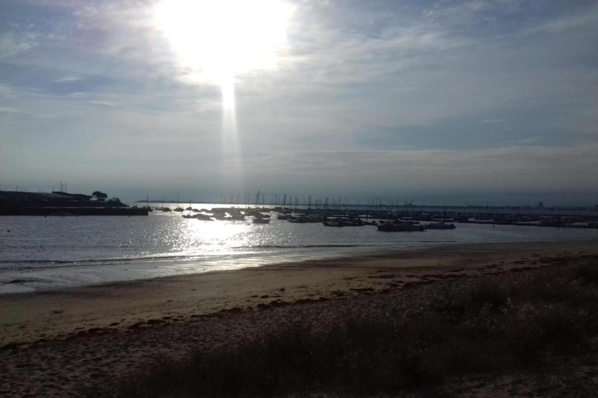 Una playa con barcos, cielo despejado y sol brillante.