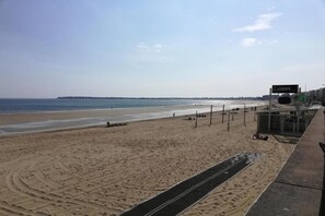 Ein Strand mit klarem Himmel, einem Schild mit der Aufschrift 'Calmos' und einem gepflasterten Weg.
