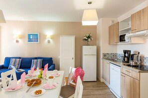 A modern kitchen with a microwave, coffee maker, and dishwasher. There is a dining area with a table set for two, and a blue sofa in the background. - Apartment in La Baule near the Beach (PORNICHET)