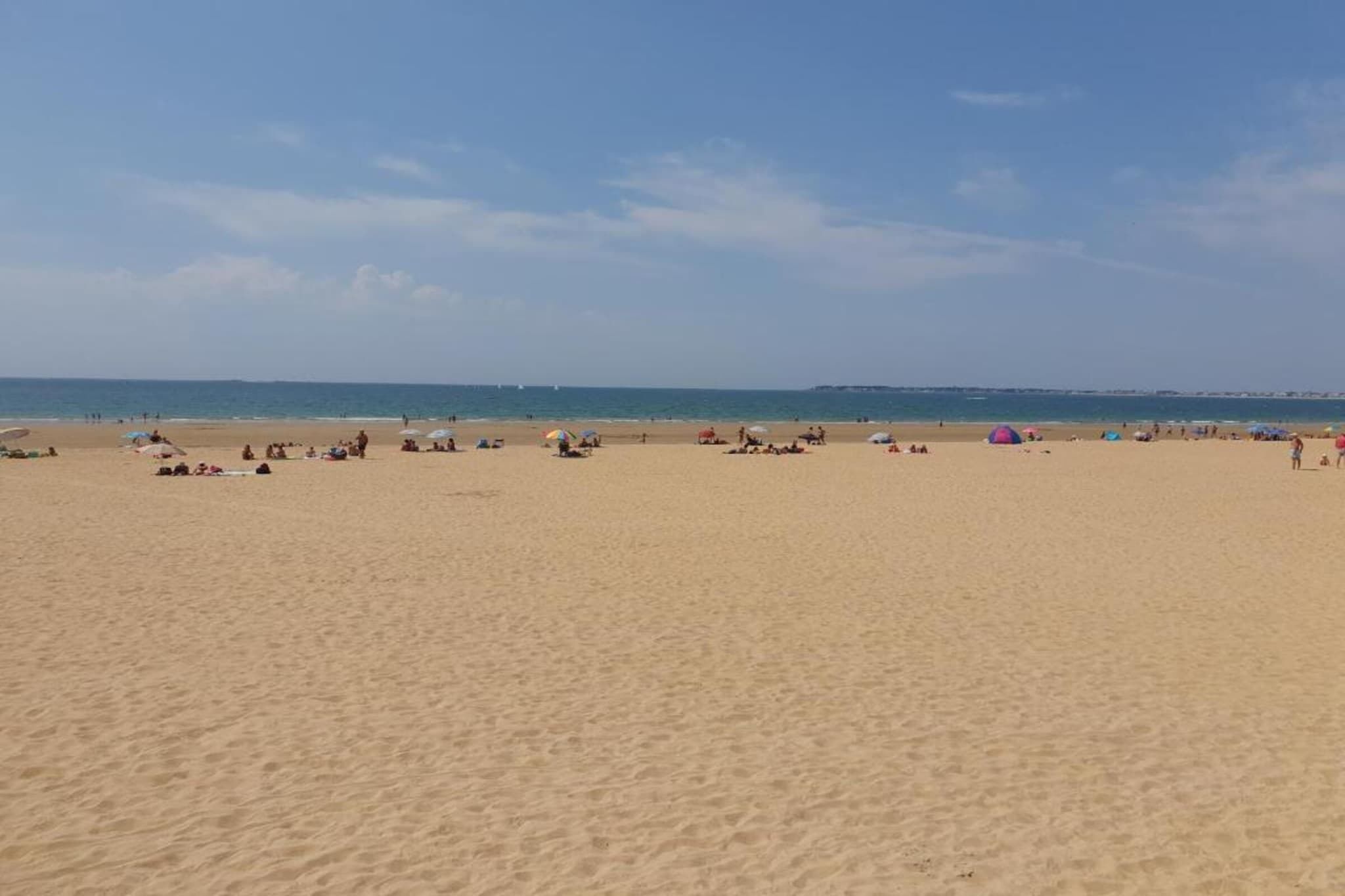 Une vaste plage de sable où l’on voit des gens et des parasols.