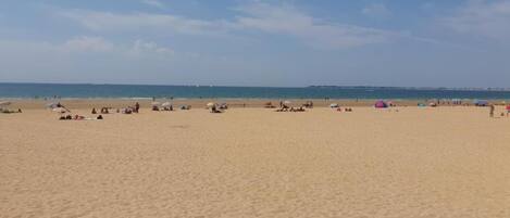 Une vaste plage de sable où l’on voit des gens et des parasols.