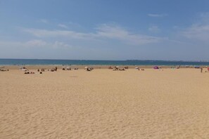 Ein weiter, sandiger Strand mit Menschen und Sonnenschirmen.