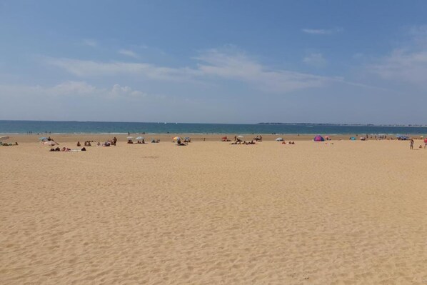 A wide sandy beach with people and umbrellas.