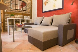 Un salon chaleureux avec un canapé d’angle, une petite table et un mur en briques.