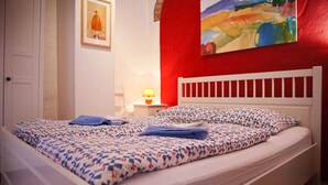 A bed with a patterned bedspread, a white headboard, and a painting on the wall. - Apartment lower deck with balcony - Gohr apartments (Stralsund)
