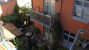 A courtyard with a metal balcony, potted plants, and a table with chairs. - Apartment lower deck with balcony - Gohr apartments (Stralsund)