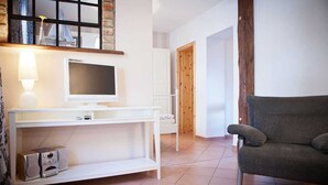 A living room with a white entertainment unit, a grey sofa, and a wooden door leading to another room. - Fewo Ostwind 1 with small terrace - Gohr apartments (Stralsund)