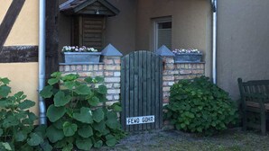 A wooden gate with a sign reading "FEWO GOHR" in front of a building with a brick wall and a window. - Fewo Ostwind 1 with small terrace - Gohr apartments (Stralsund)