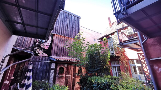 A narrow alleyway with wooden buildings, a small tree, and a metal staircase. - Villa pond view with balcony and view to the Frankenteich - Gohr apartments (Stralsund)