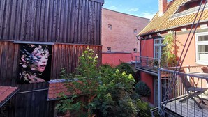A courtyard with a wooden fence, a mural, and a red building with a balcony. - Villa pond view with balcony and view to the Frankenteich - Gohr apartments (Stralsund)