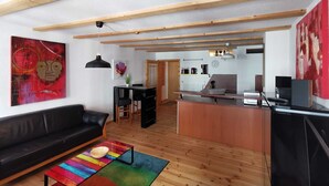 A modern living room with a black leather sofa, a colorful coffee table, and a kitchen area with wooden beams. - Villa pond view with balcony and view to the Frankenteich - Gohr apartments (Stralsund)