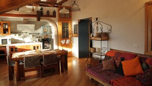 A cozy living room with a wooden dining table and chairs, a colorful sofa, and a kitchen in the background. - ESPERIA, splendid sea view and immersed in the typical greenery of the Trieste Karst (Trieste)