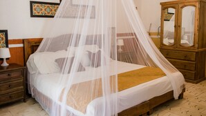 A bedroom with a bed under a canopy, a wooden wardrobe, and a nightstand with a lamp.