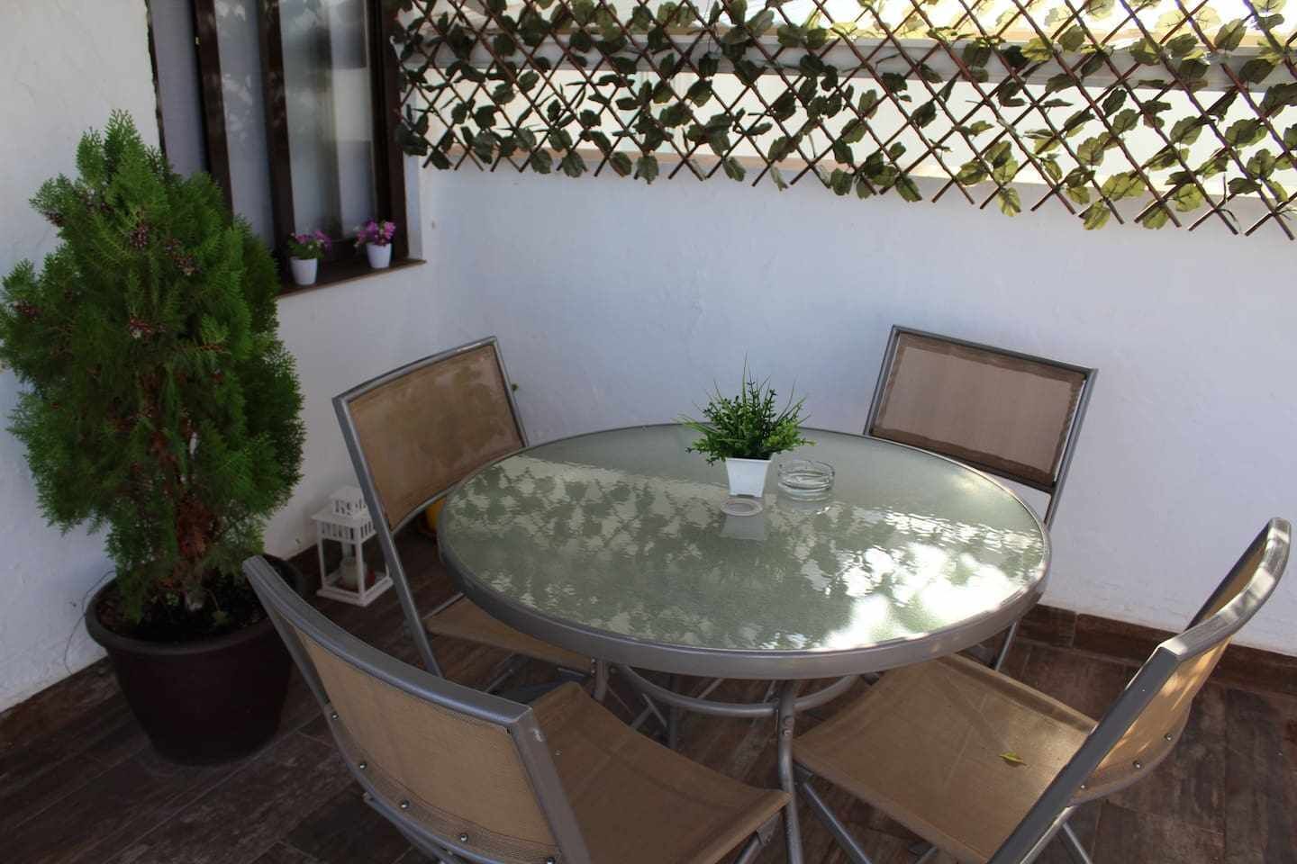 A round glass table with four chairs, a potted plant, and a decorative lattice wall.
