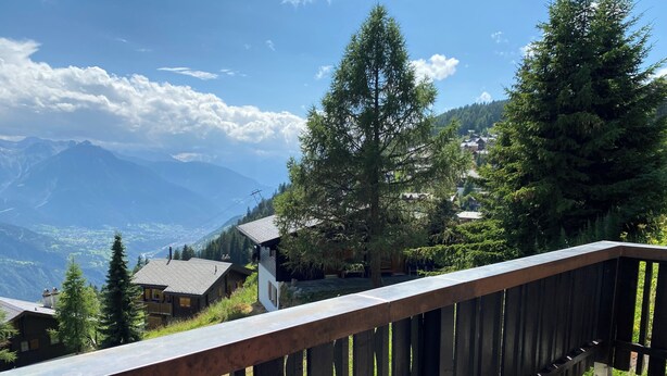 A wooden balcony overlooking a mountainous landscape with houses and trees.