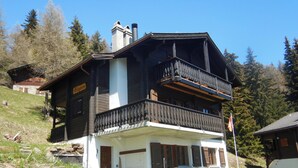 A two-story chalet with a balcony, a stone chimney, and a dining area with outdoor seating.