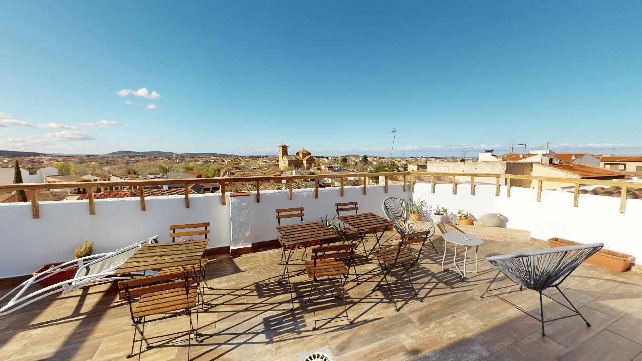 Una terraza en la azotea con mobiliario de madera y una vista despejada del paisaje circundante.