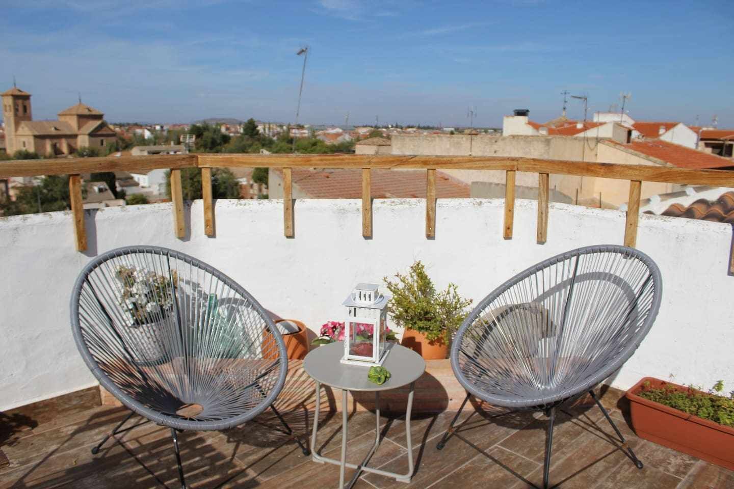 Eine Dachterrasse mit zwei Korbstühlen, einem kleinen Tisch und Topfpflanzen.
