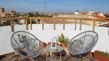 Eine Dachterrasse mit zwei Korbstühlen, einem kleinen Tisch und Topfpflanzen.