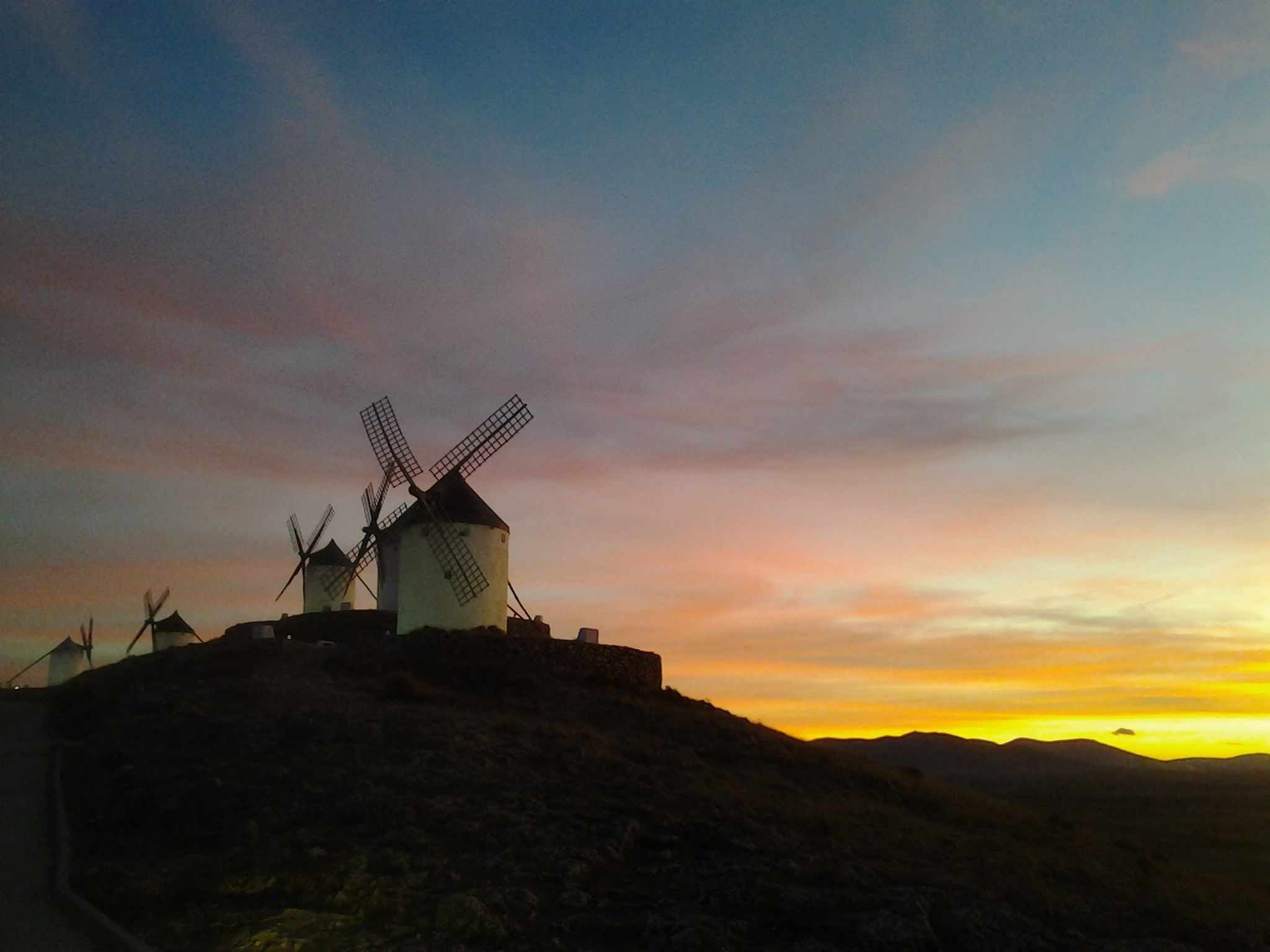 A windmill complex with multiple windmills on a hill during sunset.