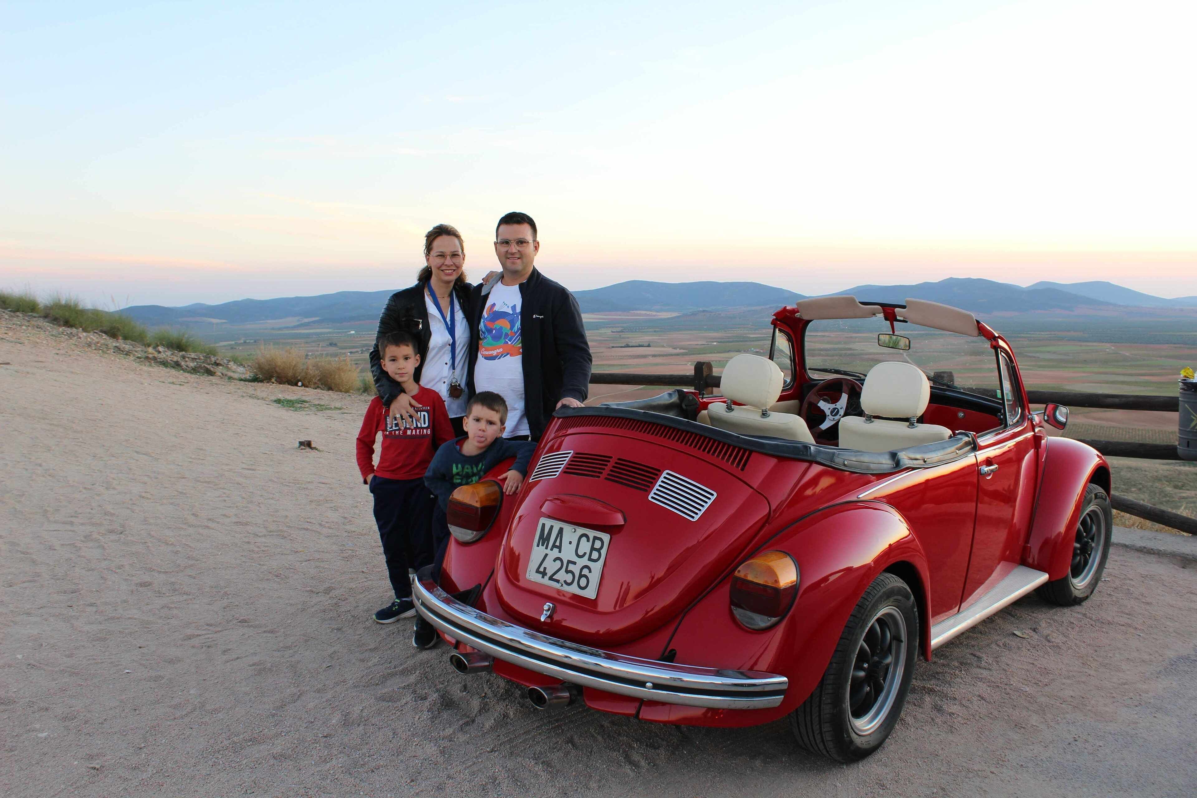 A red vintage car parked on a dirt road with a scenic view of mountains in the background.