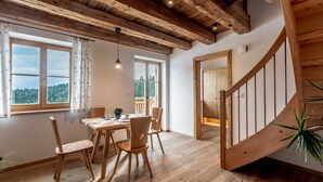 A dining area with wooden furniture, a staircase, and large windows with a view.